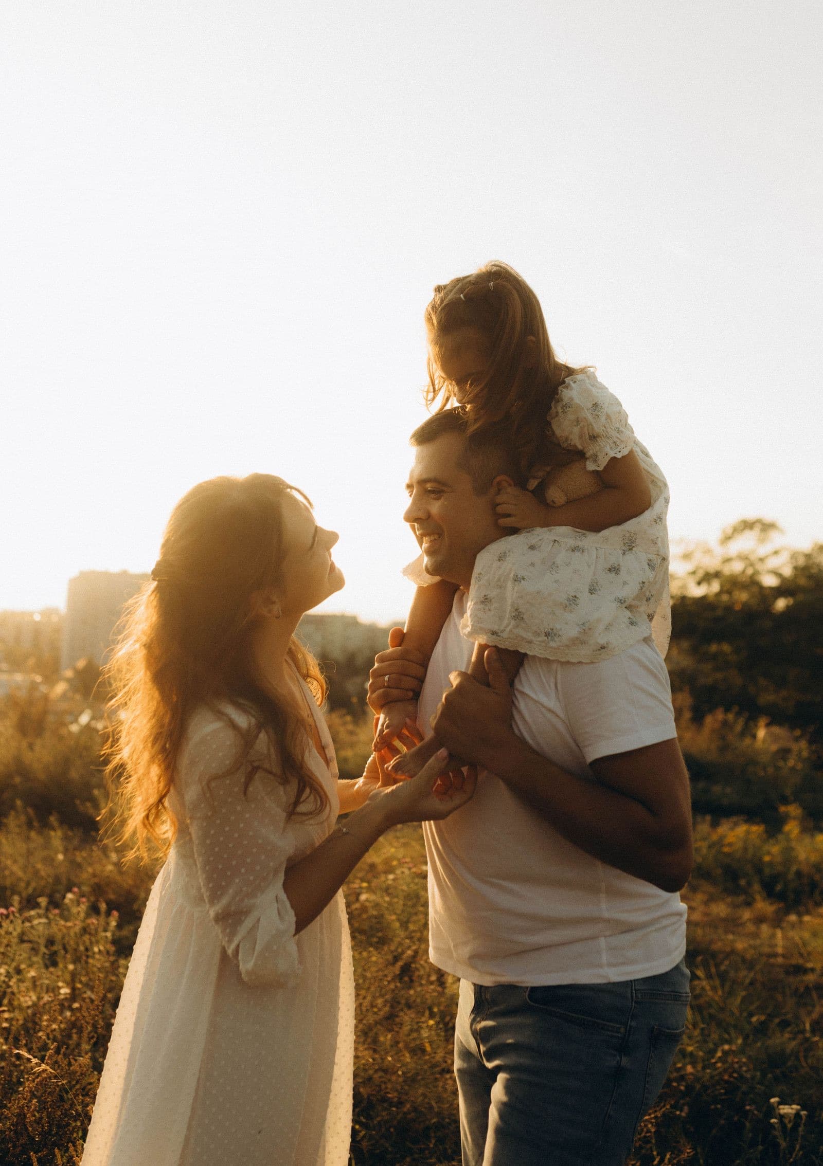 A parent carrying a child on their shoulders, laughing in warm evening light